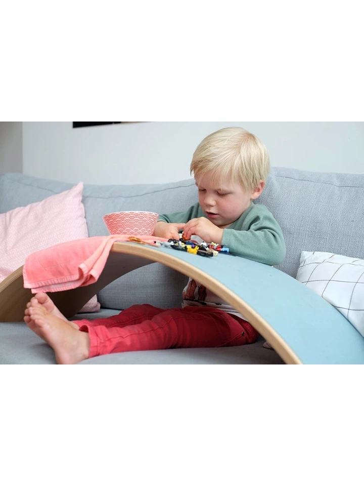 Małe dziecko na kanapie bawiące się samochodzikami na desce balansującej Wobbel.