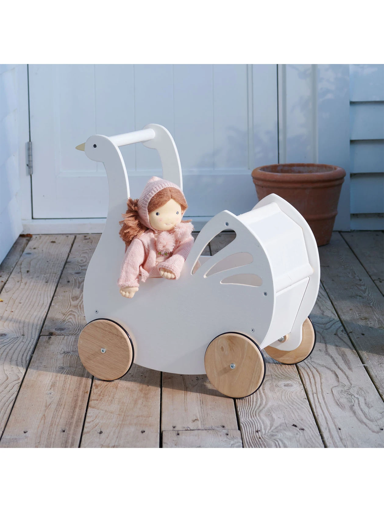Drewniany wózek dla lalek Łabędź od Tender Leaf Toys z lalką na drewnianym tarasie.