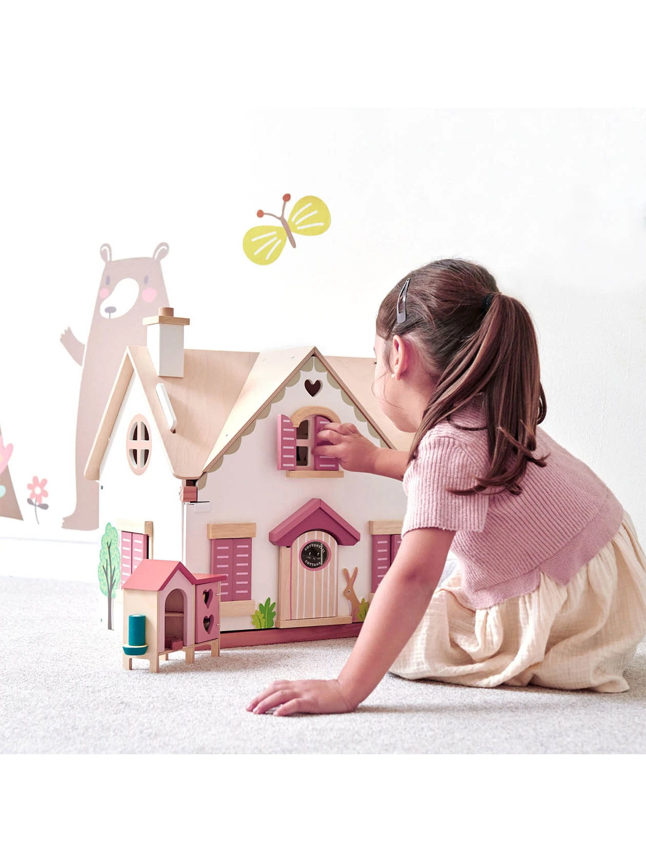 dDziewczynka bawi się drewnianym dwupietrowym domkiem dla lalek cottontail cottage od Tender Leaf Toys.