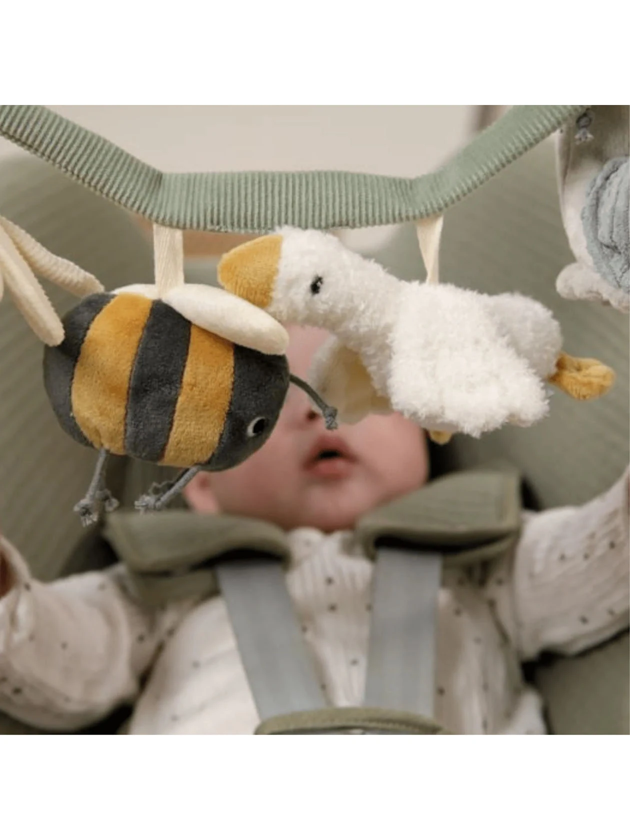 Dziecko w foteliku samochodowym patrzy na pszczołę oraz gęś, elementy zawieszki sensorycznej Little Goose marki Little Dutch.